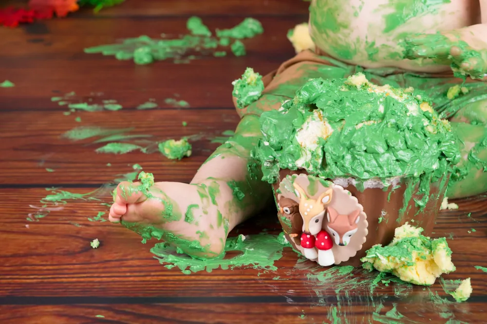 Kindje kliedert met de groene bosdieren cake smash taart op de donkere houten vloer, cakesmash fotoshoot Zoetermeer