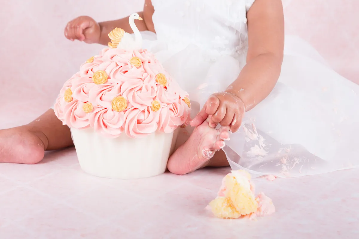 Meisje in witte jurk bij een roze taart met zwaan en gouden roosjes tijdens haar cake smash fotoshoot in Zoetermeer