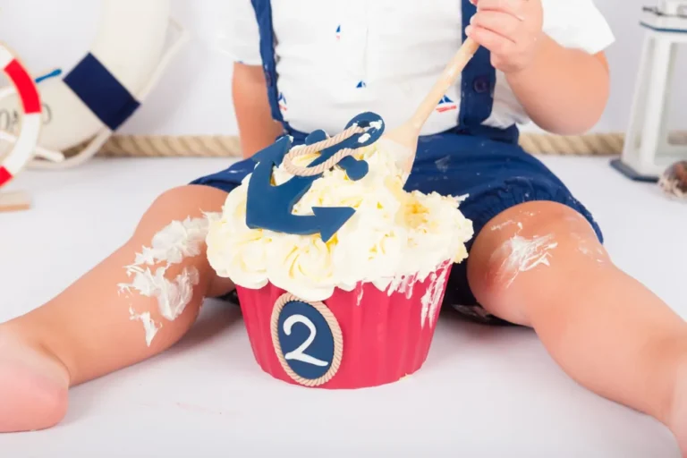 Kindje in blauwe matrozenoverall roert met een houten lepel door de maritieme cake smash taart, fotoshoot Zoetermeer