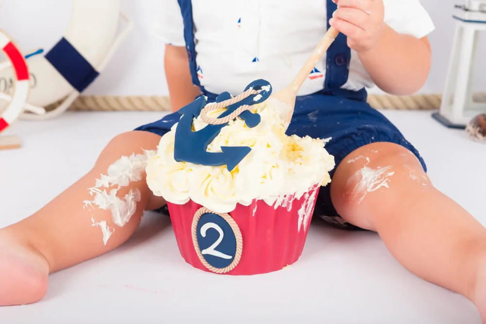 Kindje in blauwe matrozenoverall roert met een houten lepel door de maritieme cake smash taart, fotoshoot Zoetermeer