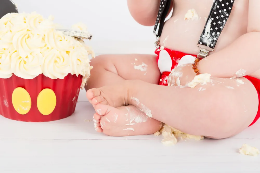 Kindje in rood broekje met bretels tussen de resten van de Mickey Mouse cake smash taart, cakesmash fotoshoot Zoetermeer