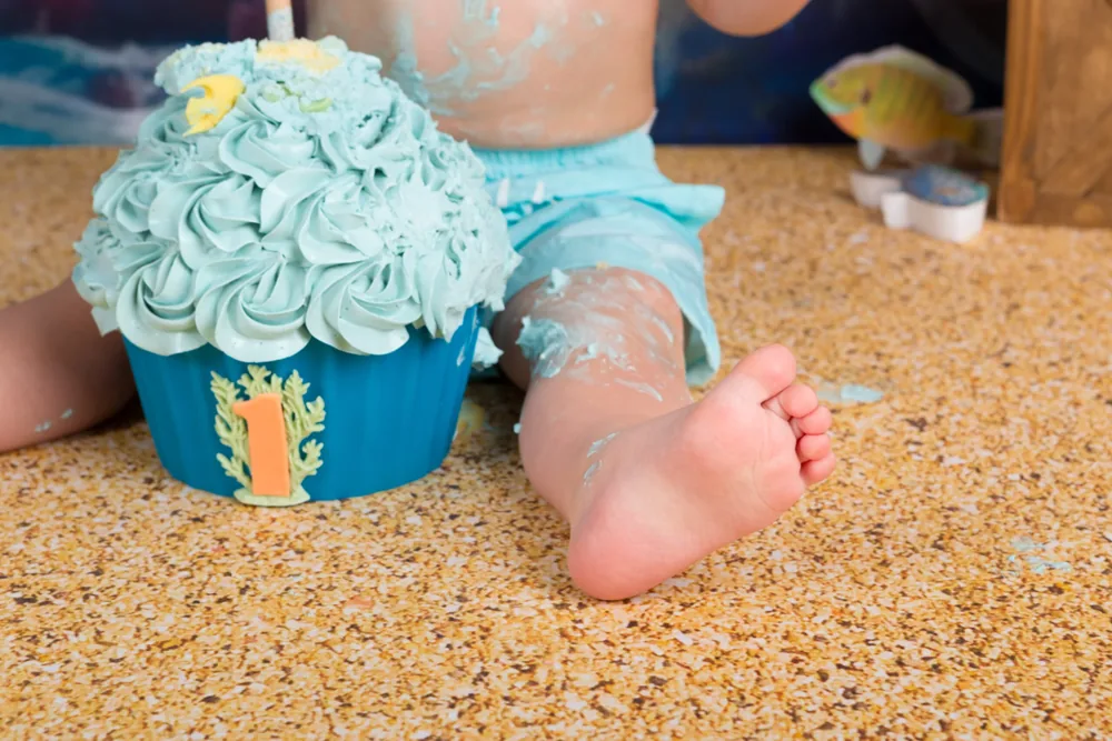 Kindje in lichtblauw broekje naast de blauwe onderwatertaart op de zandvloer, cakesmash fotoshoot Zoetermeer