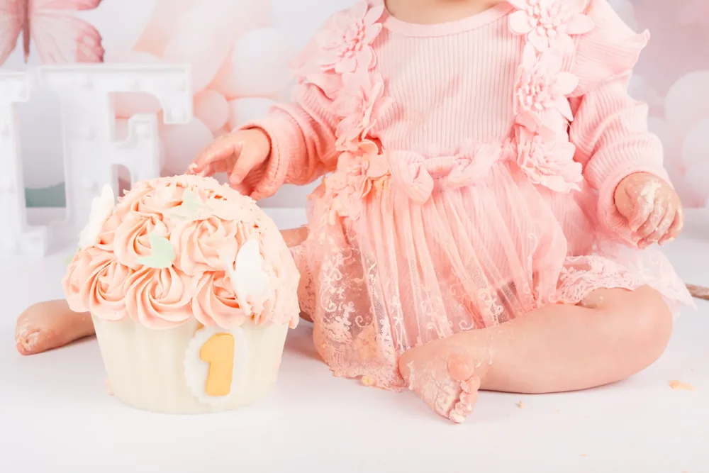 Kindje in roze jurkje met kant naast de aangesneden vlinders cake smash taart, cakesmash fotoshoot Zoetermeer