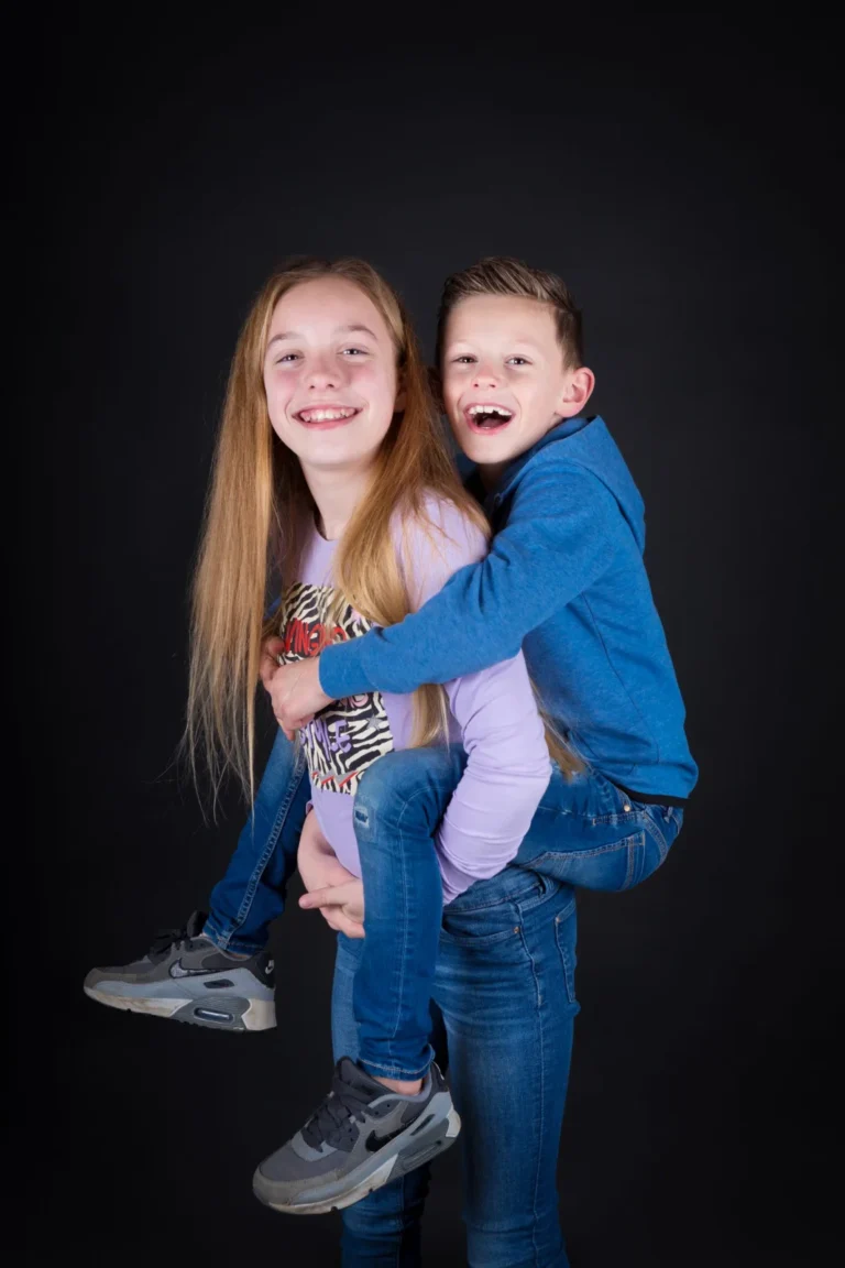 Broer springt lachend op de rug van zijn zus in de fotostudio