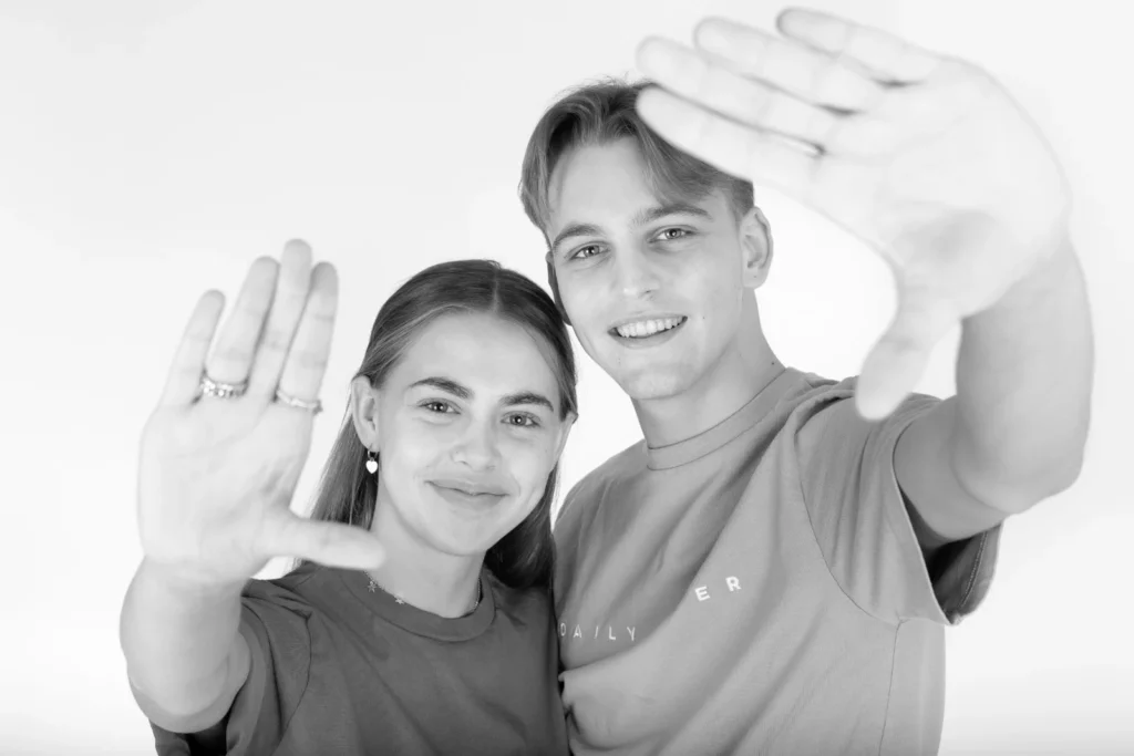 Zwart-witfoto van twee jongeren die lachend hun hand naar de camera steken