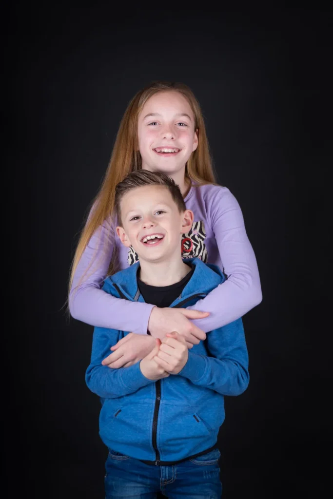 Zus omhelst haar lachende broertje tijdens een fotoshoot in de studio