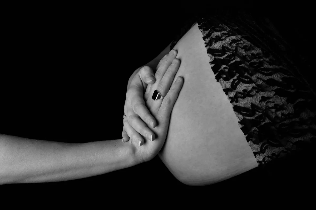 Hand op een zwangere buik met kanten stof, zwart-witfoto