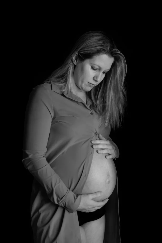 Zwart-wit zwangerschapsfoto van een vrouw die haar buik vasthoudt